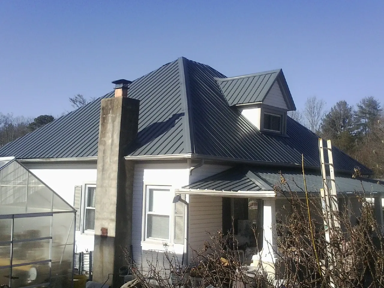 Dark blue standing seam metal roof on a white farmhouse with dormer — Slate & Tile Roof Repair by Roofing Brothers in Giltner