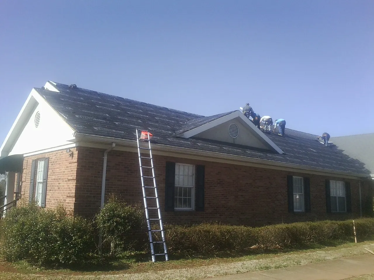 Crew tearing shingles off a brick ranch roof with a ladder set — Emergency Roof Repair work by our crew in Giltner