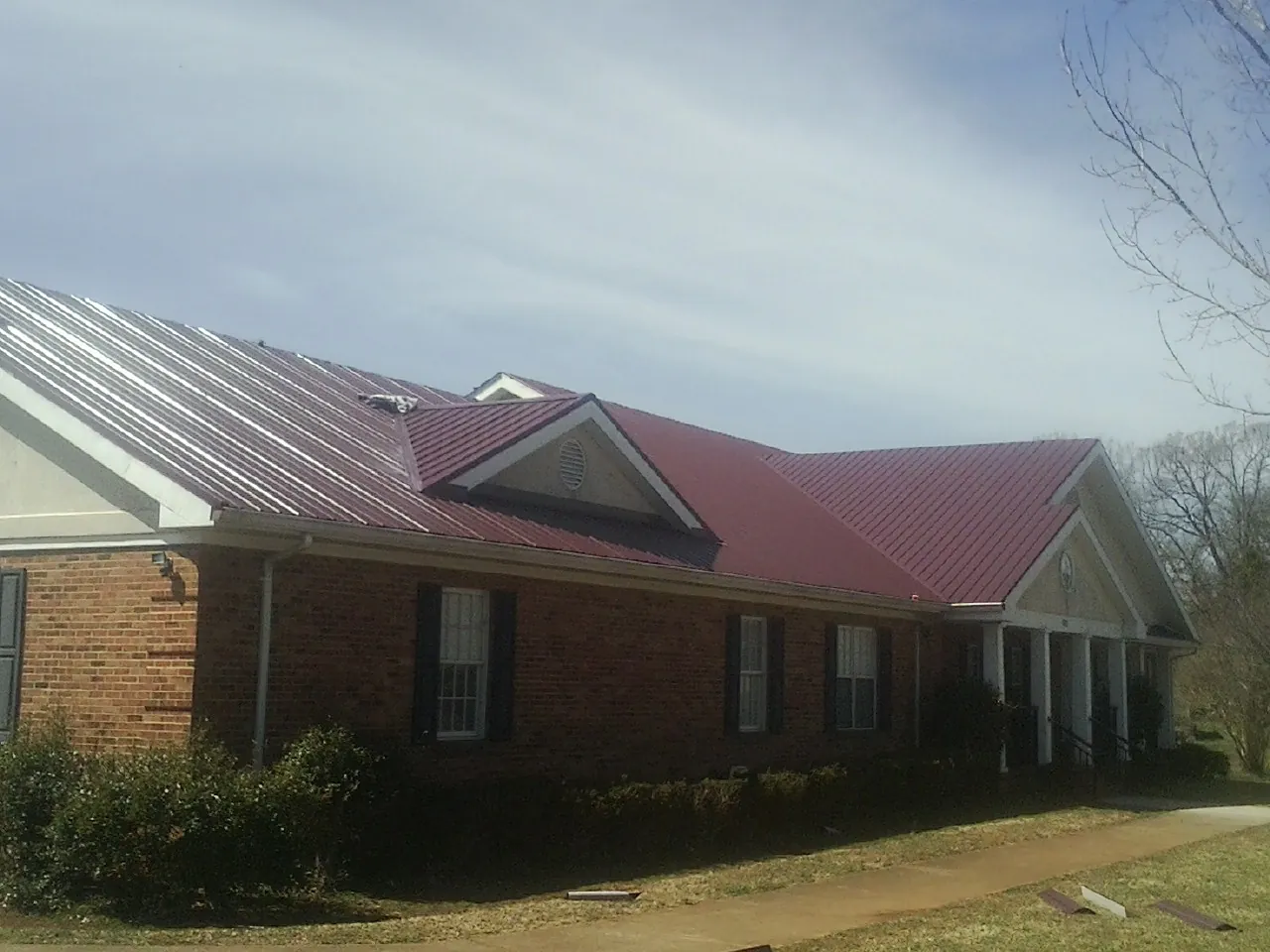 Red metal roof with gabled entries on a long brick building, from a Hail Damage Roof Repair job in Giltner
