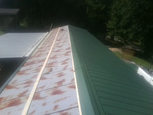 Old rusted panels beside newly installed green metal roofing — Wind Damage Roof Repair by Roofing Brothers in Giltner
