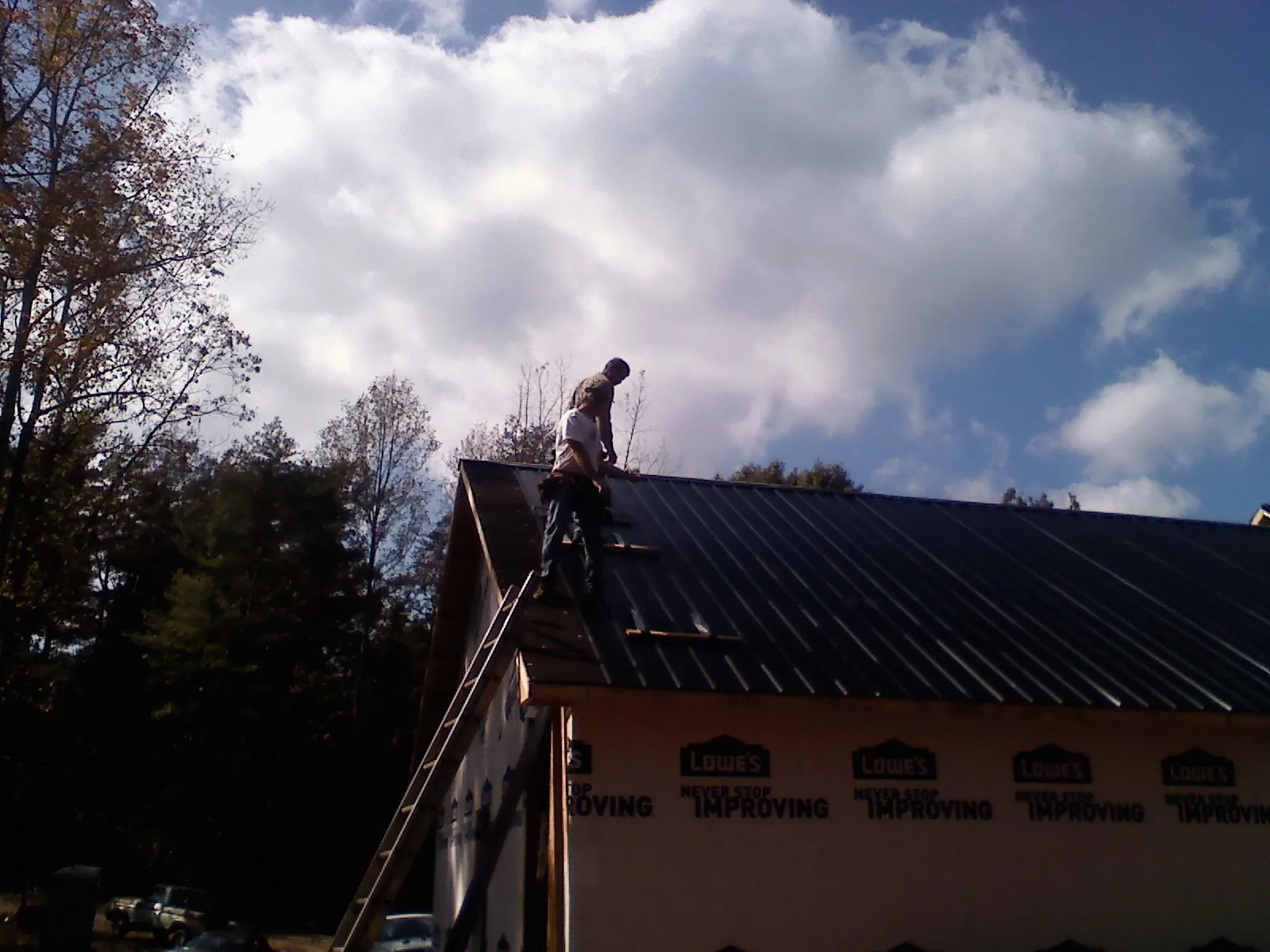 Roofer fastening dark metal panels high against a cloudy sky, from a Roof Inspection job in Giltner