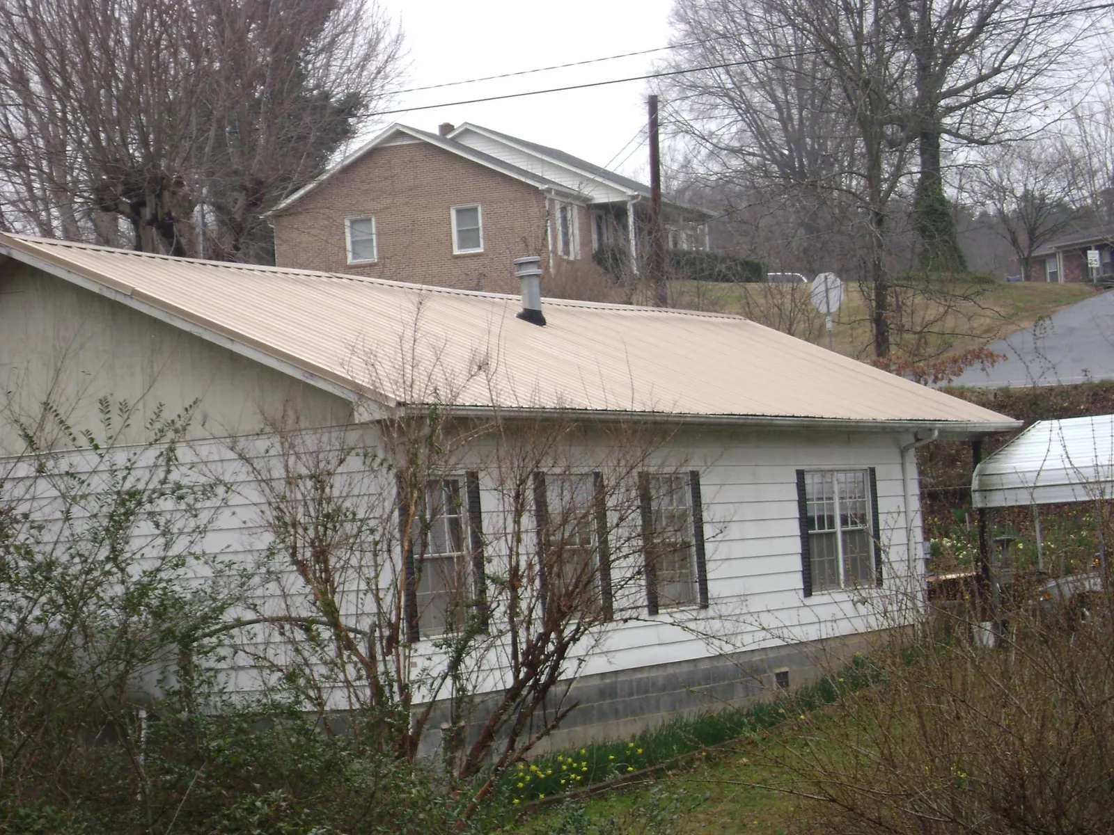 Tan metal roof on a white sided house set into a hillside — Commercial Roofing by Roofing Brothers in Giltner