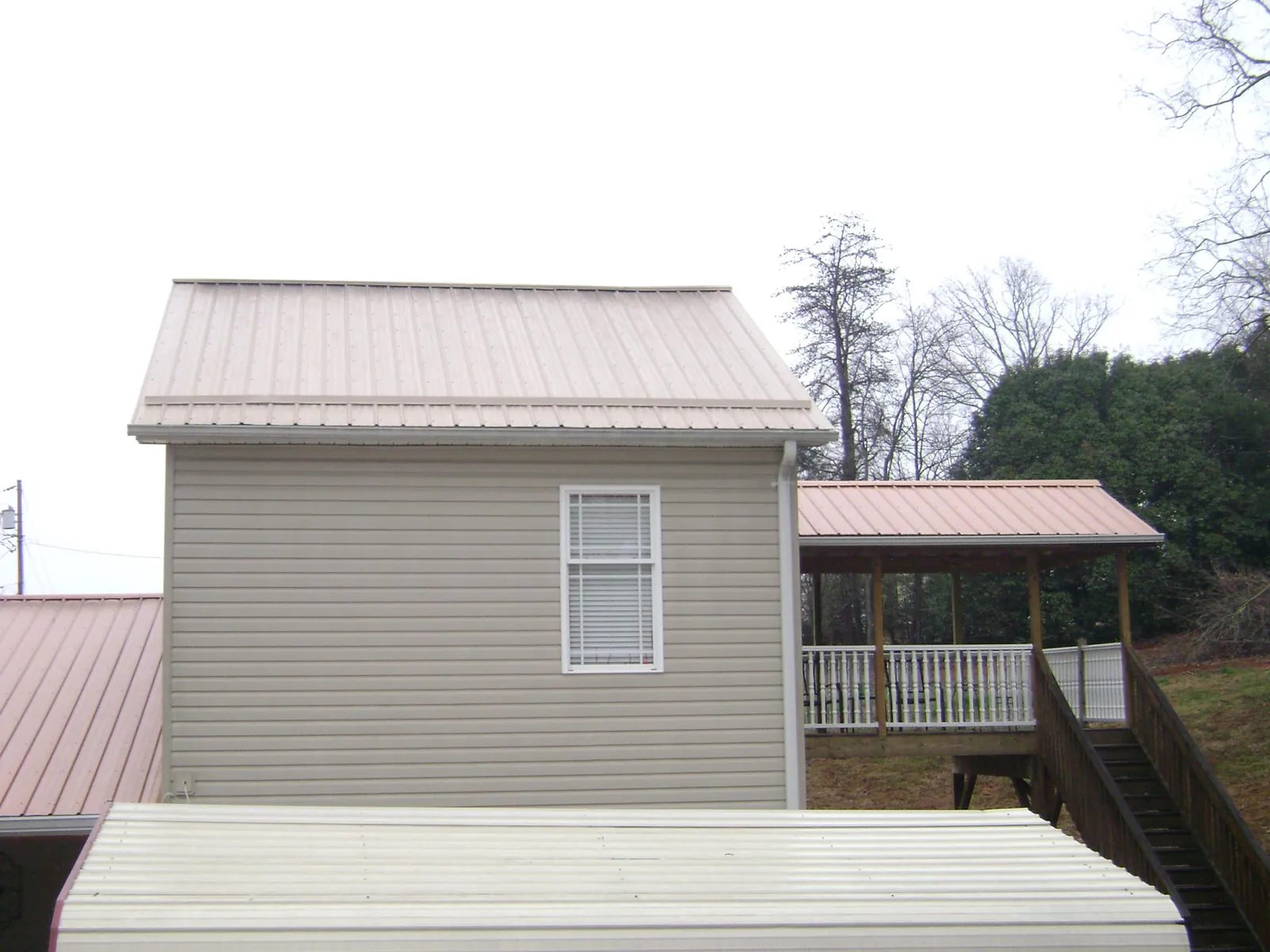 Tan metal roofs on a two story addition and attached porch, from a Roof Replacement job in Giltner